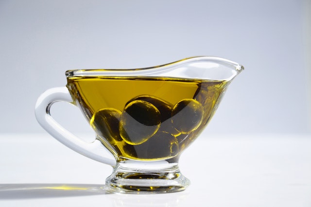 Sklenená miska s olivovým olejom a zelenými olivami